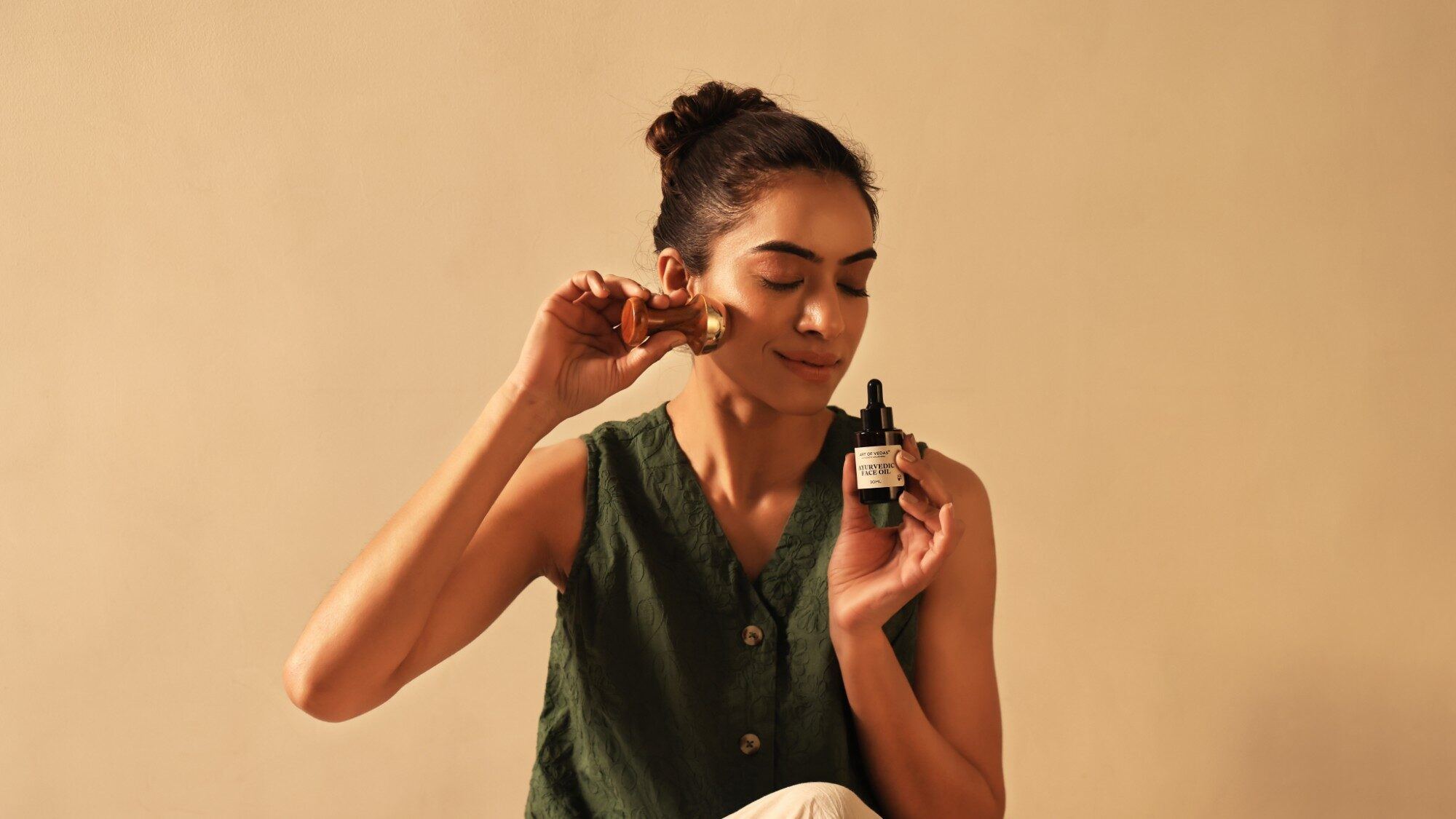 Femme passant un accessoire Kansa sur sa joue en tenant l'Huile visage ayurvédique Art of Vedas